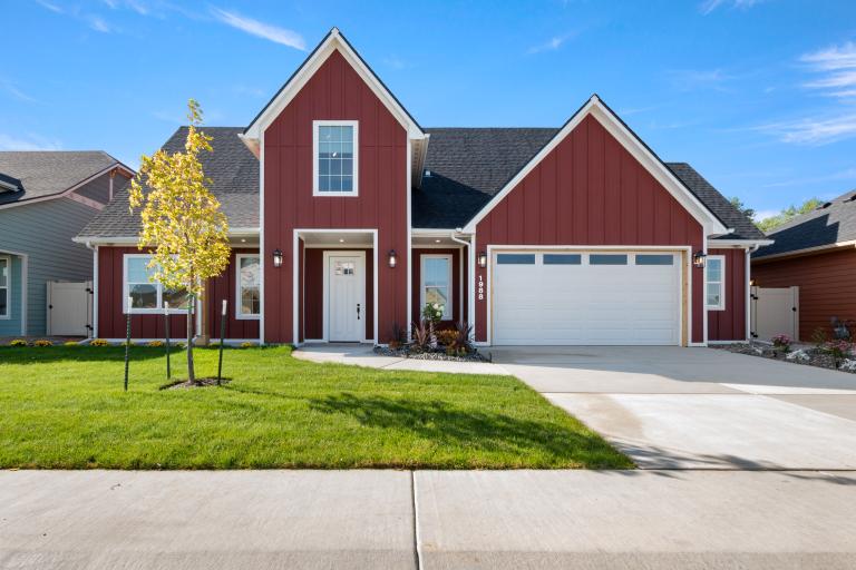 Front view of the Wellness Home from the Parade of Homes, featuring a red exterior, tall roof, and landscaped green yard. 